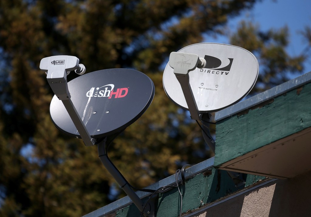 Dish TV and directv satellites are seen attached to the side of a building.